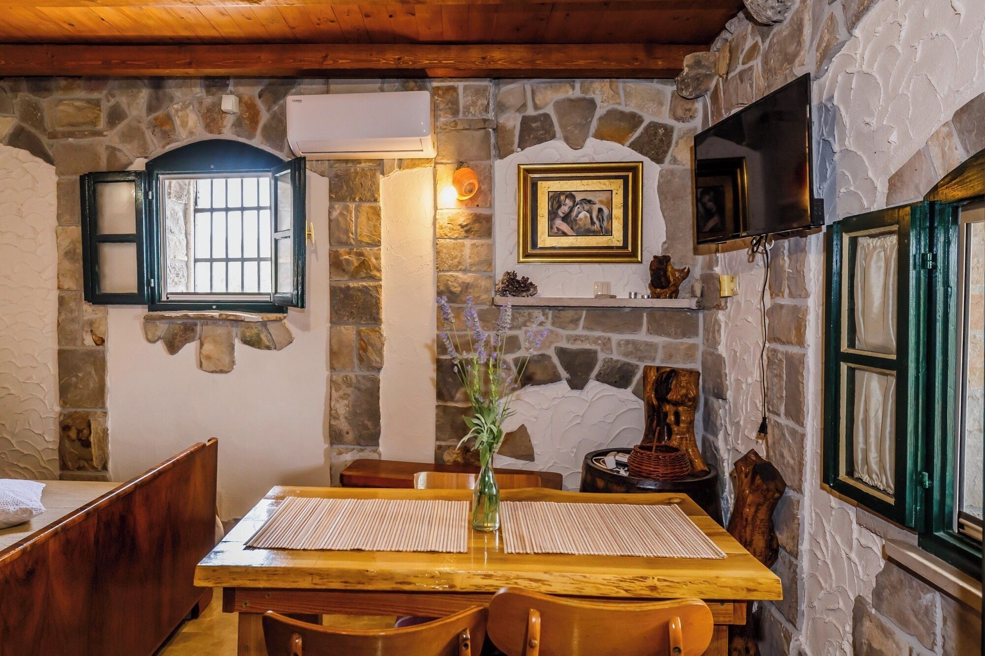 Un'area pranzo rustica con parete in pietra, travi in legno, un camino e una televisione posizionata sopra.