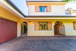 A two-story building with a paved courtyard, wooden shutters on windows, and a red garage door.