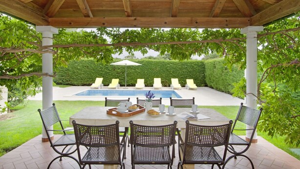 Un patio cubierto con piscina, rodeado de vegetación y amueblado para exteriores.