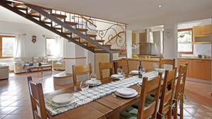 Amplia sala de estar con una mesa de comedor para seis personas, una escalera y una zona de cocina.