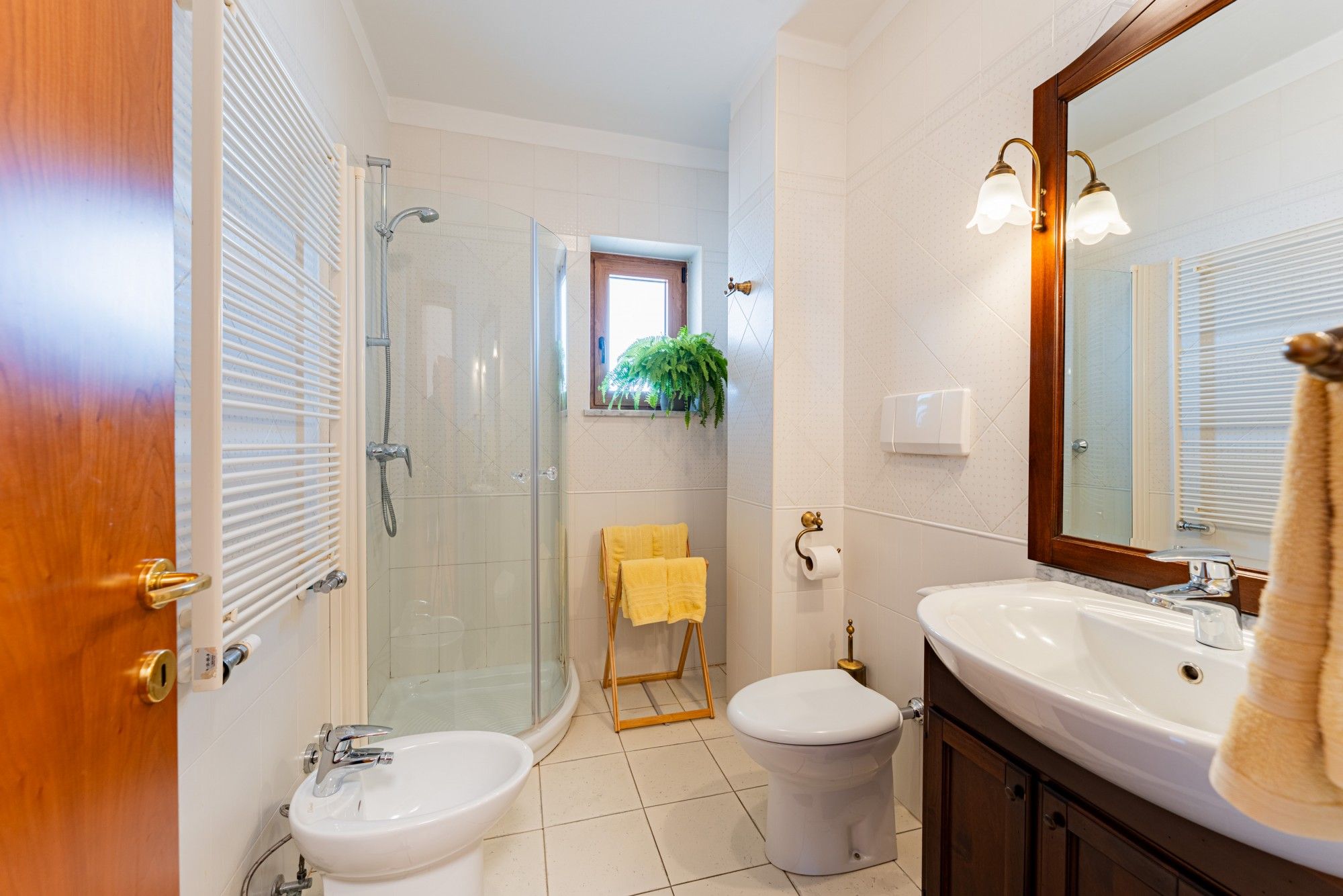 A bathroom with a glass-enclosed shower, a white sink, a toilet, and a mirror with wall-mounted lights.