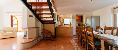 A spacious living area with a wooden staircase, a dining table with chairs, and a kitchen area with a refrigerator.
