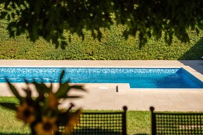 A swimming pool with a tiled edge, surrounded by a well-maintained hedge and a paved walkway.