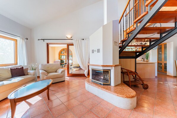 A spacious living room with a fireplace, a sofa, a coffee table, and a staircase leading to an upper level.