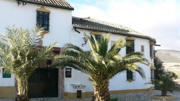 A two-story building with a white facade and yellow trim, featuring a tiled roof and multiple windows. - Cortijo la Colá - Cañete la Real, Malaga (Cañete la Real)