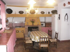 Un comedor con una mesa dispuesta para cuatro personas, una chimenea y una cocina al fondo.
