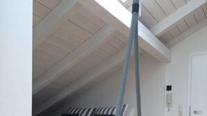 Une chambre avec un plafond en pente, un lit avec une literie à rayures, une balançoire suspendue et un plancher en bois.