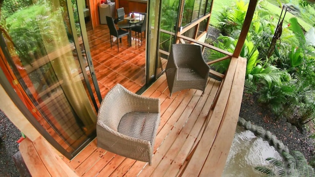 Eine gläserne Holzterrasse mit Korbstühlen, einem Esstisch und einem durch die Scheiben einsehbarer Küchenbereich.