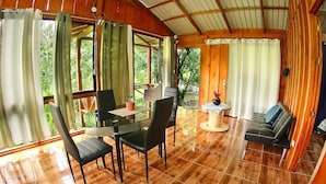 Ein Holzinterieur mit Esstisch und Stühlen, einer Couch und einem kleinen runden Tisch mit Lampe.