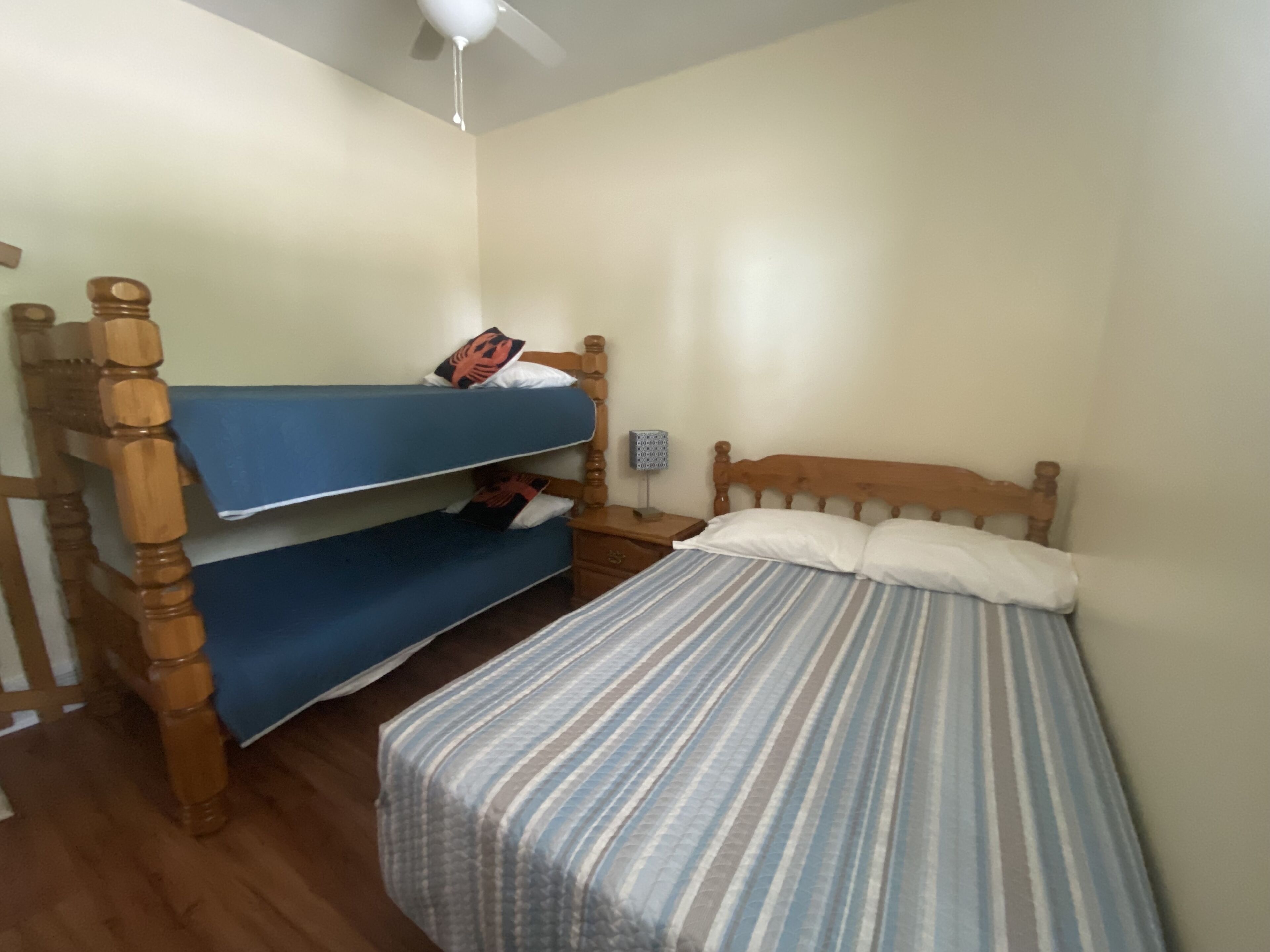 A room with a bunk bed, a single bed, wooden furniture, and a ceiling fan.