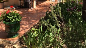 A two-story building with a balcony, a patio area with a table and chairs, and a garden with various plants. - Beautifull villa, 3,360 sq.m garden; only 1 km away from the Saint-Endréol golf club (La Motte)