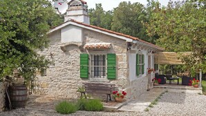 Un edifici rústic de pedra amb teulada de teules, persianes verdes i una banca a l'exterior.