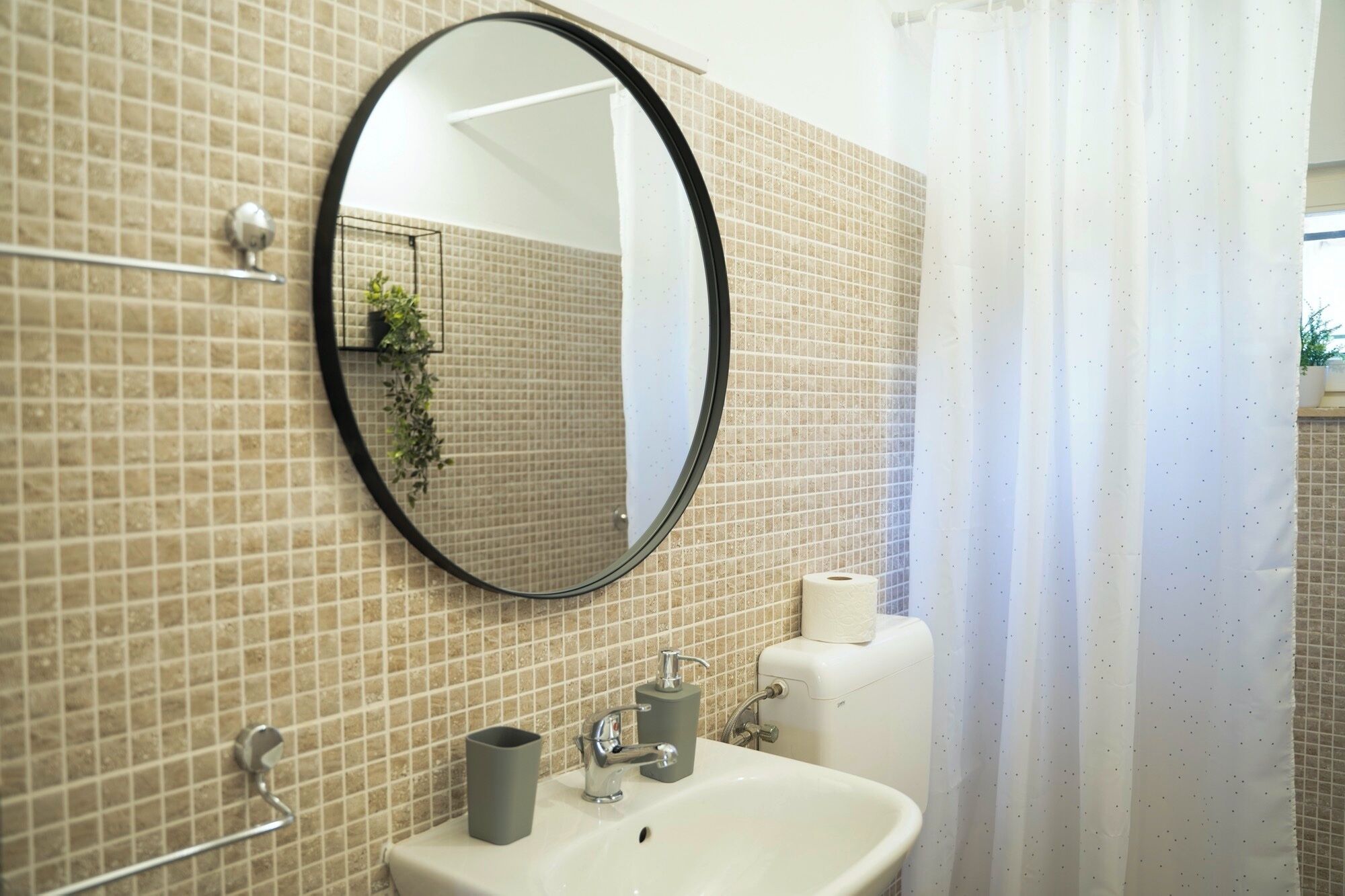 Een badkamer met een ronde spiegel, een wastafel, een toilet en een douchegordijn.