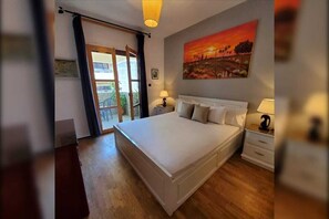 Une chambre à coucher avec un grand lit, une table de chevet, une lampe, un tableau au mur et une vue par la fenêtre.