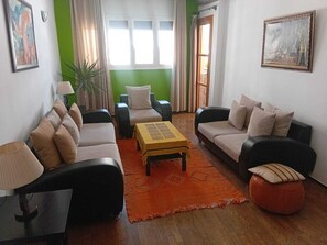 Un salon avec deux canapés, une table basse et une lampe. Il y a un mur vert et une fenêtre avec des rideaux.