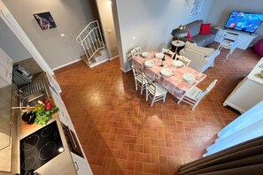 A dining area with a table set for four, a kitchen with a stove and sink, and a living area with a sofa and TV. - Borgo del Silenzio - Ginepro two-bedroom apartment with private terrace (Provincia di Pisa)