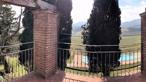 A balcony with a brick pillar, metal railing, and a view of a swimming pool and green landscape.