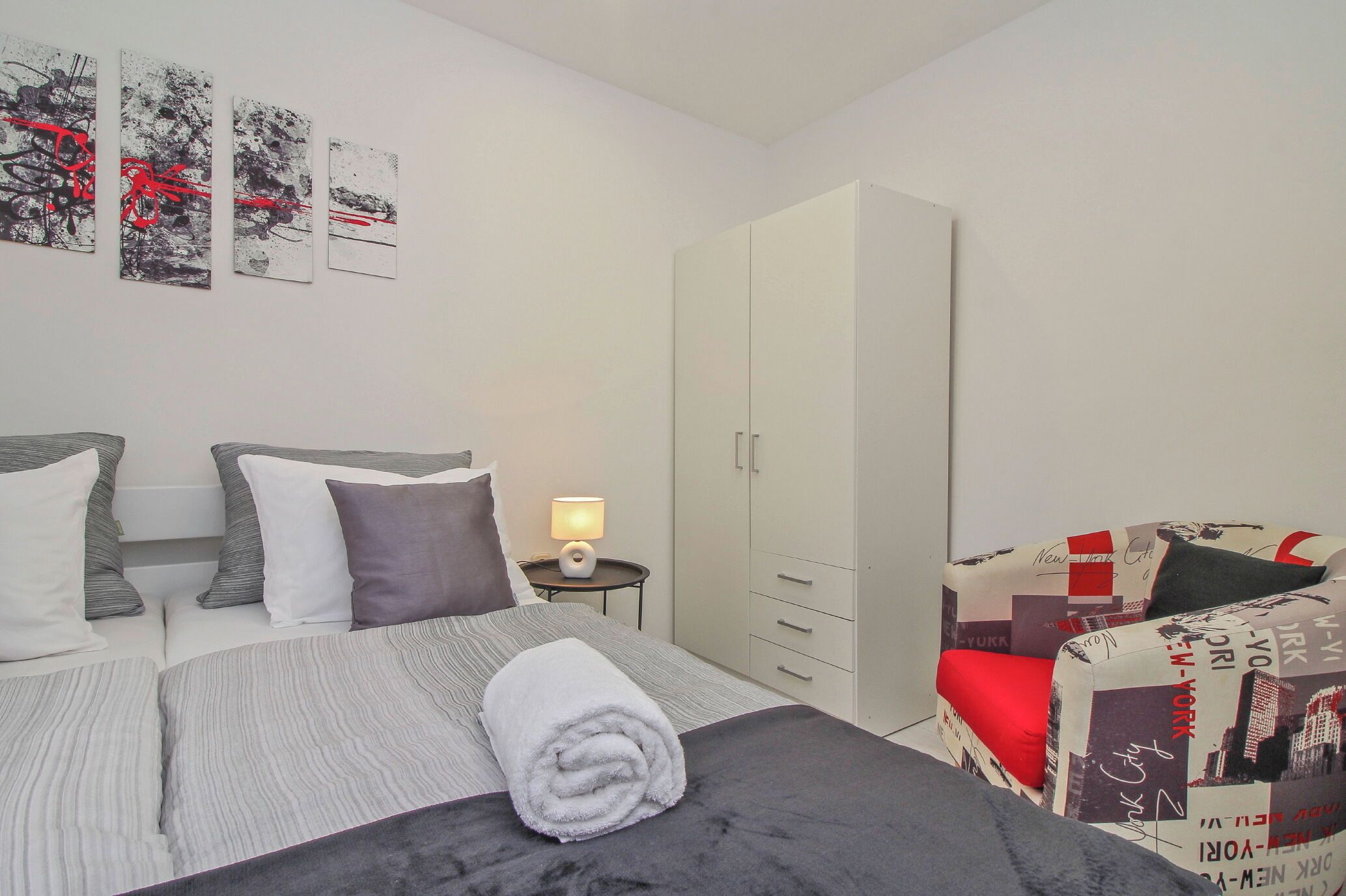Un dormitorio con cama, mesita de noche, lámpara, armario y un sofá con diseño de paisaje urbano.