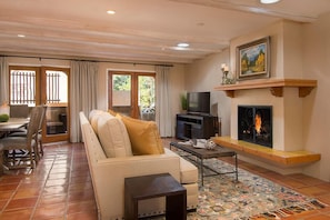 Uma sala de estar com sofá, televisão, lareira e um espaço de jantar com cadeiras e mesa.