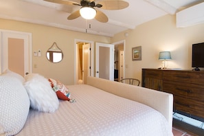 Um quarto com uma cama, um ventilador de teto, uma cômoda e uma televisão.