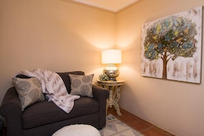 Uma sala de estar com sofá, luminária, tapete e um quadro na parede.