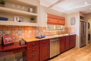 A kitchen with a wooden countertop, red cabinets, a stainless steel refrigerator, and a window with a blind.