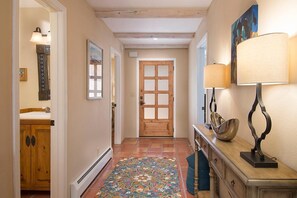 A hallway with a wooden door, a patterned rug, a wooden cabinet, and a table with a lamp.