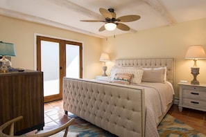 A bedroom with a tufted bed, two bedside tables with lamps, a ceiling fan, and a wooden cabinet.