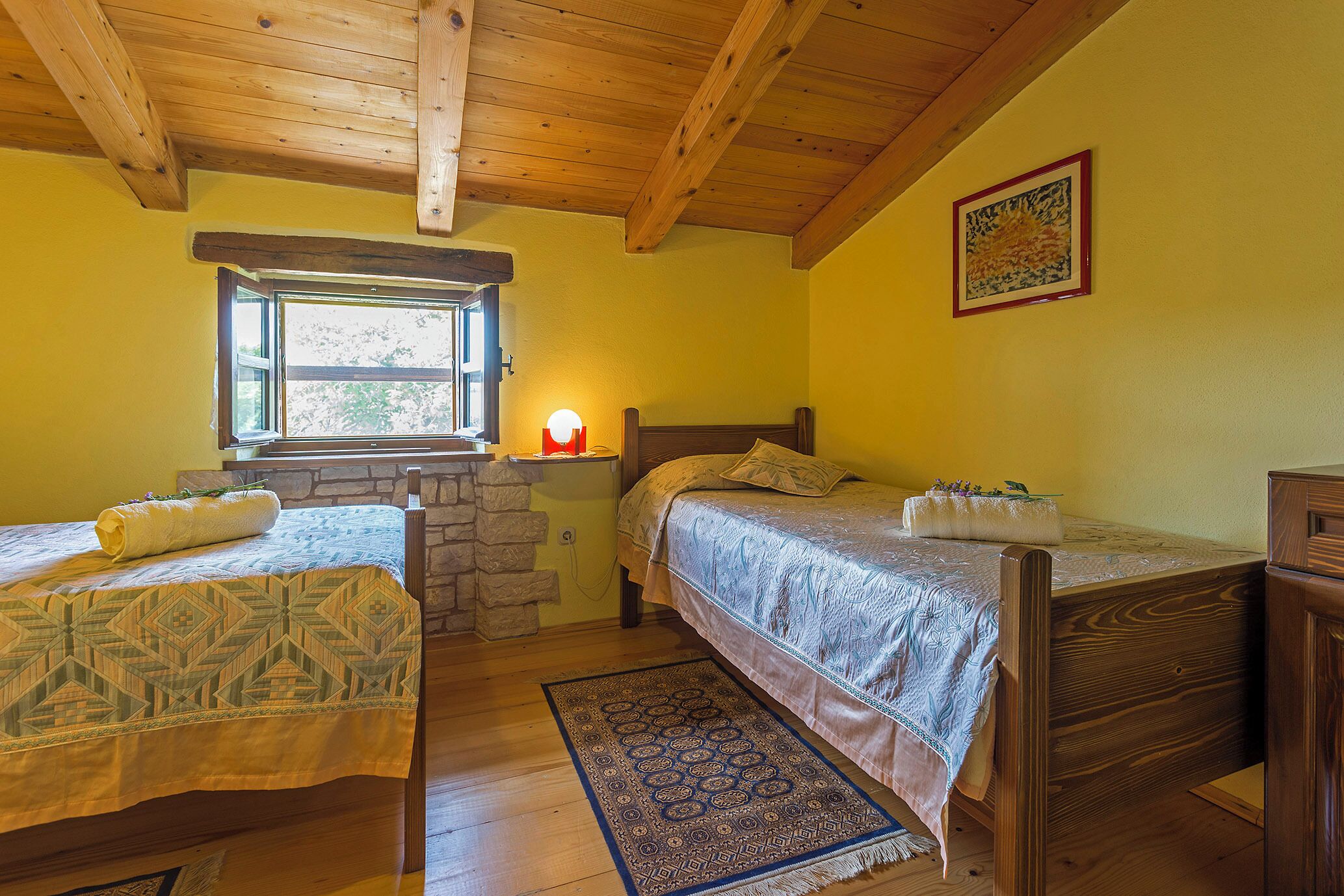 Un dormitorio con dos camas individuales, una ventana con vistas, techo de madera y pared de piedra.