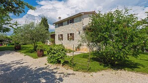 A stone house with a garden, a gravel driveway, and a clear blue sky.