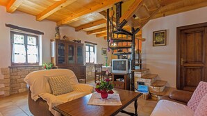 A cozy living room with a stone fireplace, wooden furniture, and a staircase leading to an upper level.