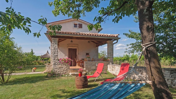 A stone house with a tiled roof, a porch, and a hammock.