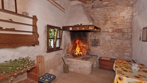 A rustic room with a stone fireplace, wooden shelves, a wooden bench, and a table with a sunflower tablecloth.