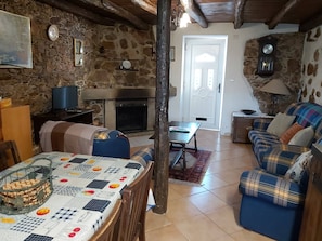 A rustic living room with stone walls, a fireplace, a dining table with a patterned tablecloth, and a plaid sofa.