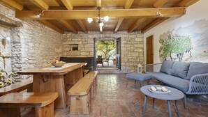 Ein rustikales Interieur mit Steinwänden, Holzbalken, einem Kamin aus Stein, einem Essbereich mit Bänken und einem Sofa.