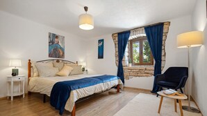 Ein Schlafzimmer mit Bett, Nachttischen, einem Sessel, einem Fenster mit Vorhängen und einem Bild an der Wand.
