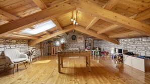 Ein gemütliches Dachzimmer mit Holzbalken, einem Kicker, einer Dartscheibe und einer Steinwand.