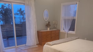 Ein Schlafzimmer mit Holzboden, einem Bett, einer Kommode und einem Fenster mit durchsichtigen Vorhängen.