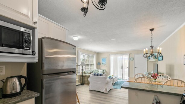 A modern kitchen with a stainless steel refrigerator, a microwave, and a kettle. There is a dining area with a table and chairs, and a chandelier above. - Walk To Beaches, Main Street, and Harbor. 1BR Cottage. Quiet Area. Captain Gosnold Village 18A (Hyannis)