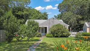 A house with a front porch, a stone pathway leading to the door, and a small garden with flowers. - Walk To Beaches, Main Street, and Harbor. 1BR Cottage. Quiet Area. Captain Gosnold Village 18A (Hyannis)
