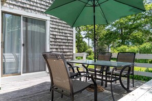 Eine Terrasse im Freien mit Tisch, Stühlen und einem grünen Sonnenschirm, sowie einer Schiebeglastür.