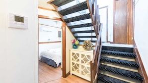 Un escalier dont les marches sont décorées de motifs à pois noirs et blancs, menant à une chambre à coucher où se trouvent un lit et une table de chevet.