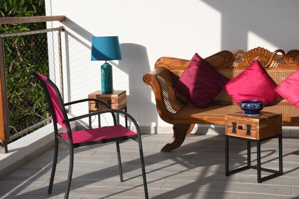 A balcony with a wicker sofa, a red chair, a small table with a lamp, and a bowl. - MORINGA 4 to 6 pers Pool and magnificent view (SAINT PIERRE)