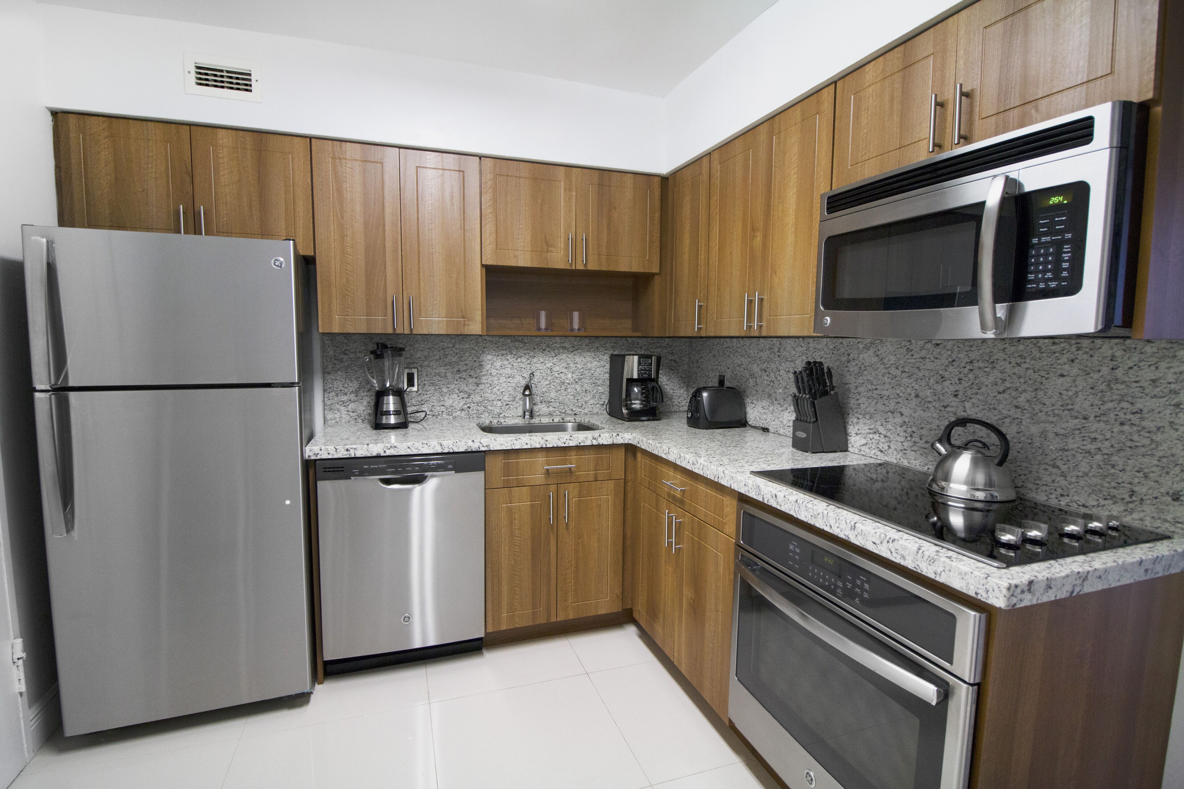 A modern kitchen with stainless steel appliances, wooden cabinets, granite countertops, and a built-in oven.