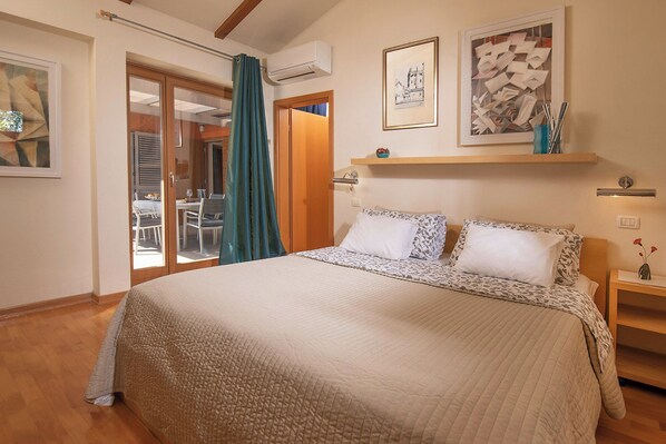 A bedroom with a large bed, a wooden floor, a sliding glass door leading to a balcony, and a small table with a vase. - Villa Emili in Medulin (Haus für 4-5 Personen) (Medulin)