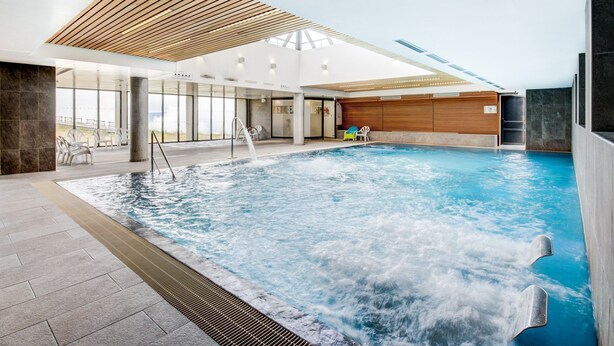 Une piscine intérieure avec un plafond en bois et une vue sur l’extérieur.