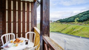 Un balcon avec une table préparée pour le petit-déjeuner, donnant sur une colline verdoyante et une route.