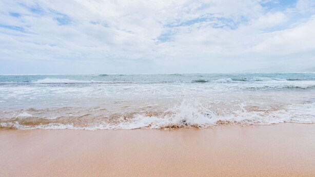 A beach with waves approaching the shore under a partly cloudy sky.