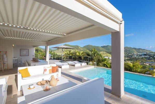 A modern outdoor pool area with a view of mountains, a covered seating area, and a dining space.