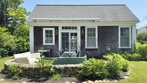 A two-story house with a dark shingled roof, white trim, and a front porch with a table and chairs. - Stylish In-Town Cottage- Walk to everything! (Vineyard Haven)